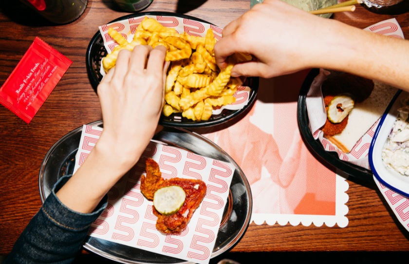 Hands reaching for fried chicken at Belles Hot Chicken Bondi.