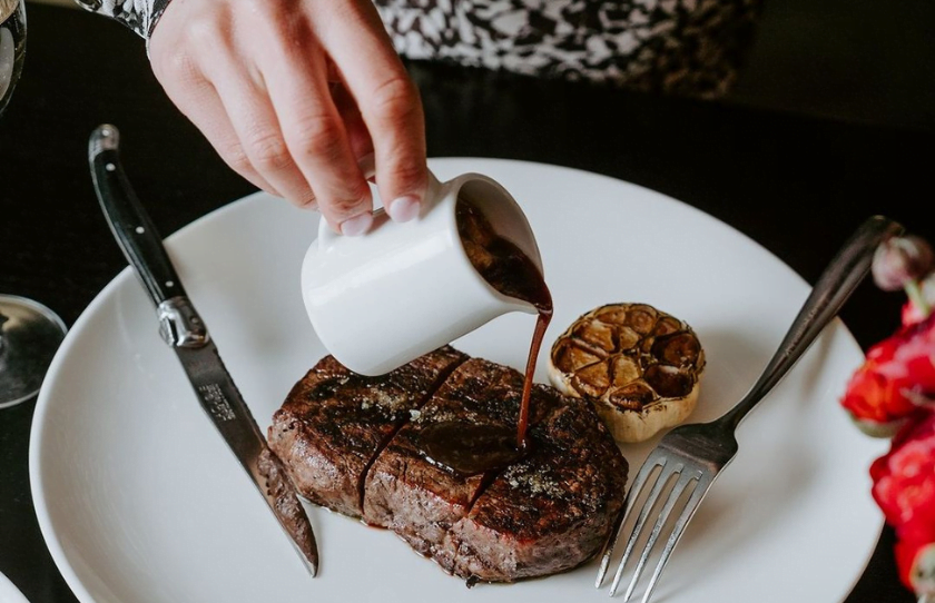 Jus being poured over medium rare steak at Botswana Butchery.