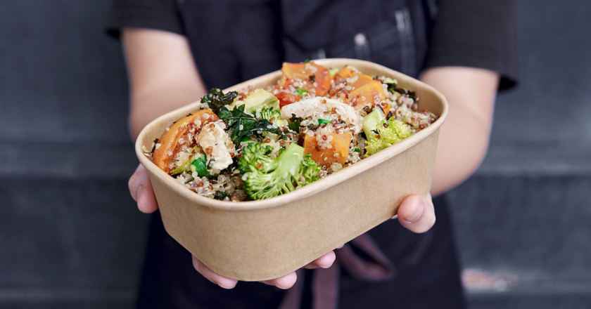 Girl in black apron holding the winter salad in a brown paper box