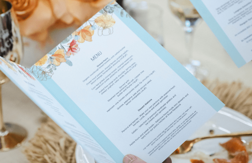 woman holding a menu with flowers in the background. menu is a shared style and includes desert station for Sydney Everest carnival long lunch at the Australian Turf Club.