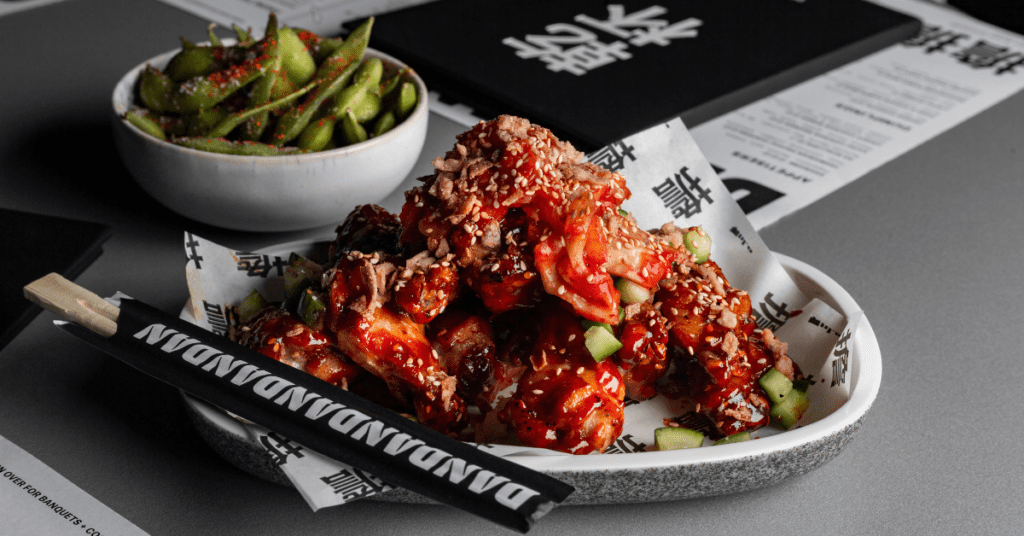 Image of chicken dish with edamame beans on a white plate and Dan Dan chopsticks