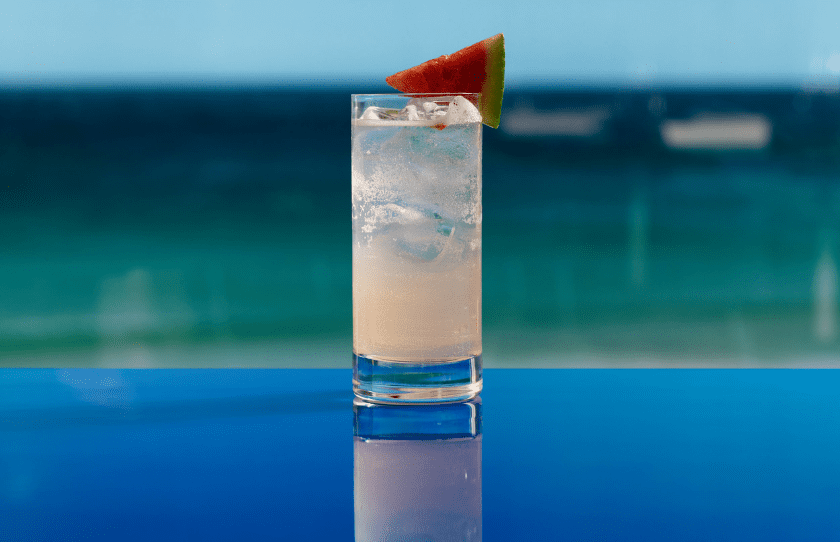 Melon cocktail on blue table with the ocean in the background curated by Beverage Director Brendon Hill